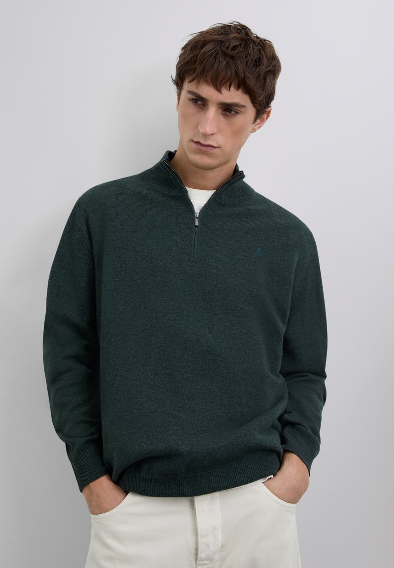 Dunkelgrüner Pullover aus weichem Strickstoff, mit einem Reißverschluss am Kragen und langen Ärmeln. Minimalistisches Design ohne sichtbare Muster.