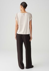 Beige, losvallend topje met korte mouwen en een sleutelgatdetail aan de achterkant, gecombineerd met donkere, wijde, gestructureerde broeken. Glad materiaal.