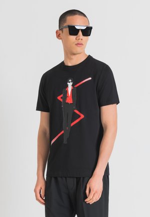 Camiseta negra con estampado gráfico de una figura en un traje rojo y gafas de sol, acentuada por una línea en zigzag roja. Corte casual, material de algodón.