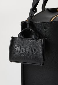 Zwarte leren handtas met een kleine bijpassende DKNY leren pouch, bevestigd met een bandje en details in goudkleurig metaal.