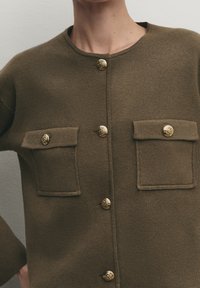 Olive green knit cardigan with a round neckline, featuring two chest pockets and gold decorative buttons along the front.