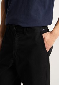 Black denim pants with a classic fit, featuring a front pocket and a button closure. The fabric appears sturdy and textured.