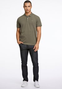 Oliven grøn polo t-shirt med krave og tre knapper, parret med mørkeblå jeans og hvide sneakers. Simpelt design, glat tekstur.