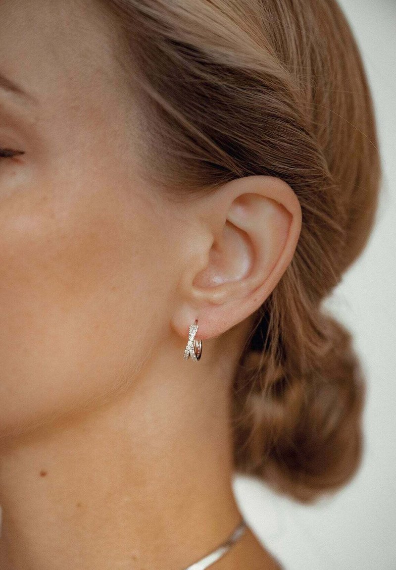 Orecchini a cerchio di piccole dimensioni con una finitura in oro rosa lucido, intrecciati con un cinturino in argento testurizzato decorato con pietre chiare.