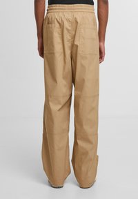 Beige wide-leg pants with a textured fabric, elastic waistband, and two large back pockets. Style features visible stitching and a loose fit.