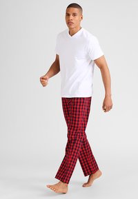 Camiseta blanca de manga corta y escote en V combinada con pantalones de pijama de cuadros rojos y negros. Los pantalones tienen un corte recto y una textura de tela suave.