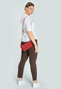 Borsa a tracolla rossa in pelle con finitura testurizzata. Presenta una forma rettangolare sottile con una lunga tracolla regolabile e accenti in metallo.