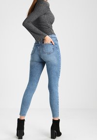 Jeans ajustados azules con un lavado desgastado, cintura alta y bolsillos traseros, combinados con una blusa a rayas negra y gris y botas negras de tobillo.