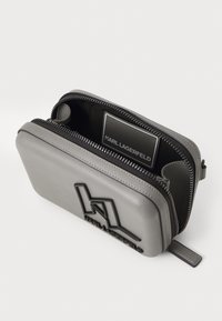 Pochette in pelle grigia con zip, dettagli con logo in rilievo, forma strutturata e zip nera a contrasto. L'interno presenta un'etichetta del brand.