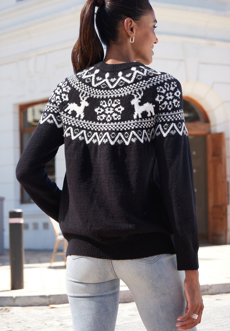 Schwarzer Pullover mit einem weißen Fair-Isle-Muster mit Rentieren und Schneeflocken über der Schulterpartie, gestrickte Textur sowie gerippte Bündchen und Saum.