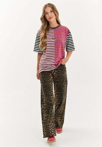 Pasiasta, oversize koszula w różowo-czarnym kolorze z motywem motyla, w połączeniu z brązowymi spodniami w panterkę i różowymi butami casualowymi.