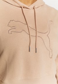 Felpa beige con un contorno cucito del logo di un puma che salta e coulisse beige con punte metalliche.