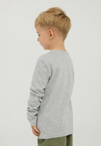Maglietta grigia a maniche lunghe in cotone. Design semplice con scollo tondo e spacchi laterali, abbinata a pantaloni verdi.