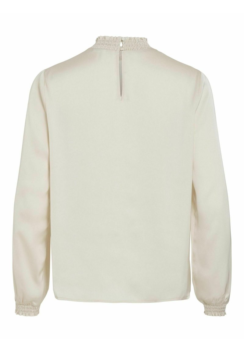 Blouse beige clair à manches longues, avec un col smocké et une fermeture à bouton en forme de trou de serrure à l'arrière. Tissu doux et lisse avec une teinte neutre.