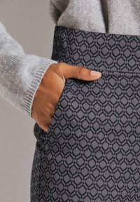 Textuur, donkergrijze stof met een geometrisch patroon; close-up van een hand in de broekzak van een patroonrok, gecombineerd met een lichtgrijze trui.