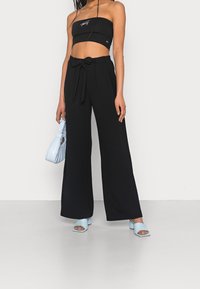 Top negro sin tirantes, pantalones negros de pierna ancha con cintura con cinturón, bolso azul claro y sandalias a juego con tacón ancho. Tejido suave, ajuste estructurado.