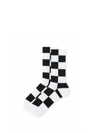 Paire de chaussettes montantes à motif damier noir et blanc, étalées à plat sur un fond blanc.
