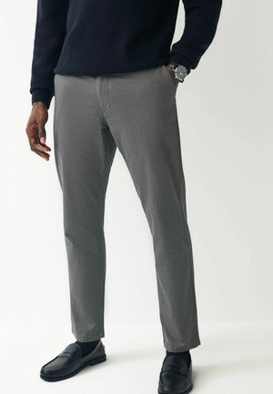 Graue maßgeschneiderte Hosen mit glatter Textur und geradem Schnitt, kombiniert mit schwarzen Slippern und einem marineblauen Pullover.
