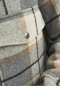 Tessuto a scacchi di lana nei toni grigi, crema e marrone; con un accento di bottone e una texture morbida, caratterizzato da un design strutturato.