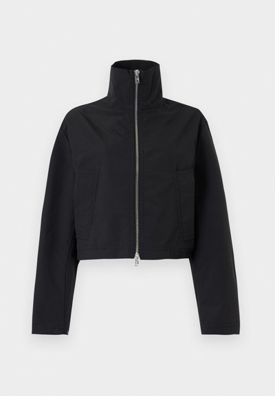 Μαύρο cropped τζάκετ με ψηλό γιακά και ασημί φερμουάρ μπροστά, με μακριά μανίκια και δύο εμπρόσθιες τσέπες σε μονόχρωμο φόντο.