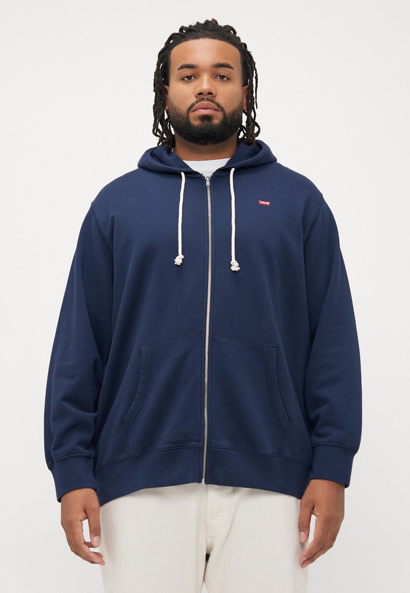 Felpa con zip navy in misto cotone con due tasche frontali, cordini bianchi e un piccolo logo sulla parte superiore sinistra del petto. Taglio regolare.