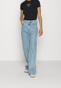 Ljusblå vida jeans i denim med hög midja och kontrasterande sömmar. Matchas med en svart t-shirt med vit logotext.