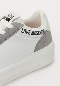 Valged ja hallid tennisetossud, mis on valmistatud nahast ja suede'ist, mis on varustatud tekstuurse pinnaga, ümmarguse ninaga ning "LOVE MOSCHINO" brändimisega kandadel.