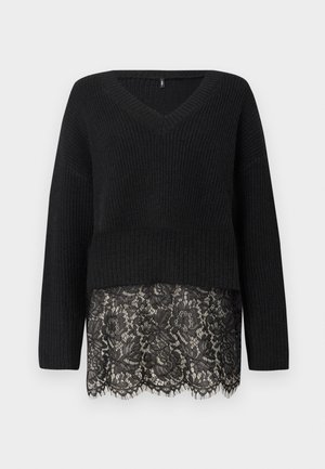 Sort striktrøje med V-hals, der har lange ærmer og en scalloped blondekant. Den teksturerede stof kontrasterer med den glatte blonde nedenfor.