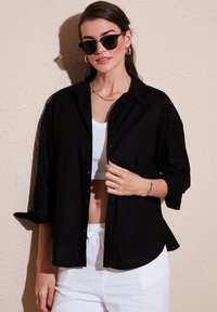Black button-up shirt with three-quarter length sleeves, lightweight fabric, soft texture, paired with a white crop top and light pants.