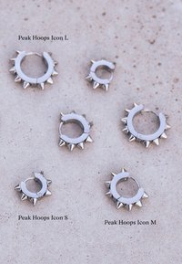 Metalinės žiedinės auskarai trijų dydžių (S, M, L) su aštriais, smailiais akcentais. Atspindinčio sidabro paviršius, apvalios formos ir uždara konstrukcija.