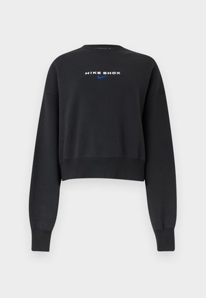 Sweat-shirt noir cropé à manches longues avec poignets et ourlet côtelés, arborant le texte blanc "NIKE SHOX" et un swoosh Nike bleu sur la poitrine.