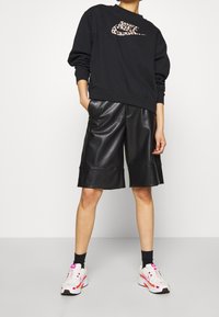 Zwarte sweatshirt met een panterprint Nike-logo. Gecombineerd met hoge zwarte nep-lederen shorts en sportieve witte sneakers.