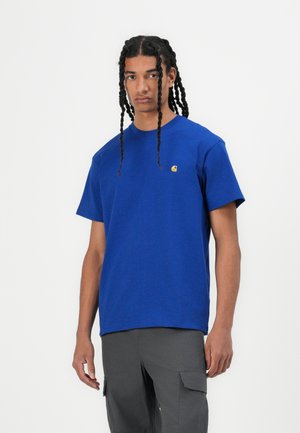 T-shirt en coton bleu à manches courtes, avec un petit logo jaune sur la poitrine gauche. Texture lisse et design classique à col rond.