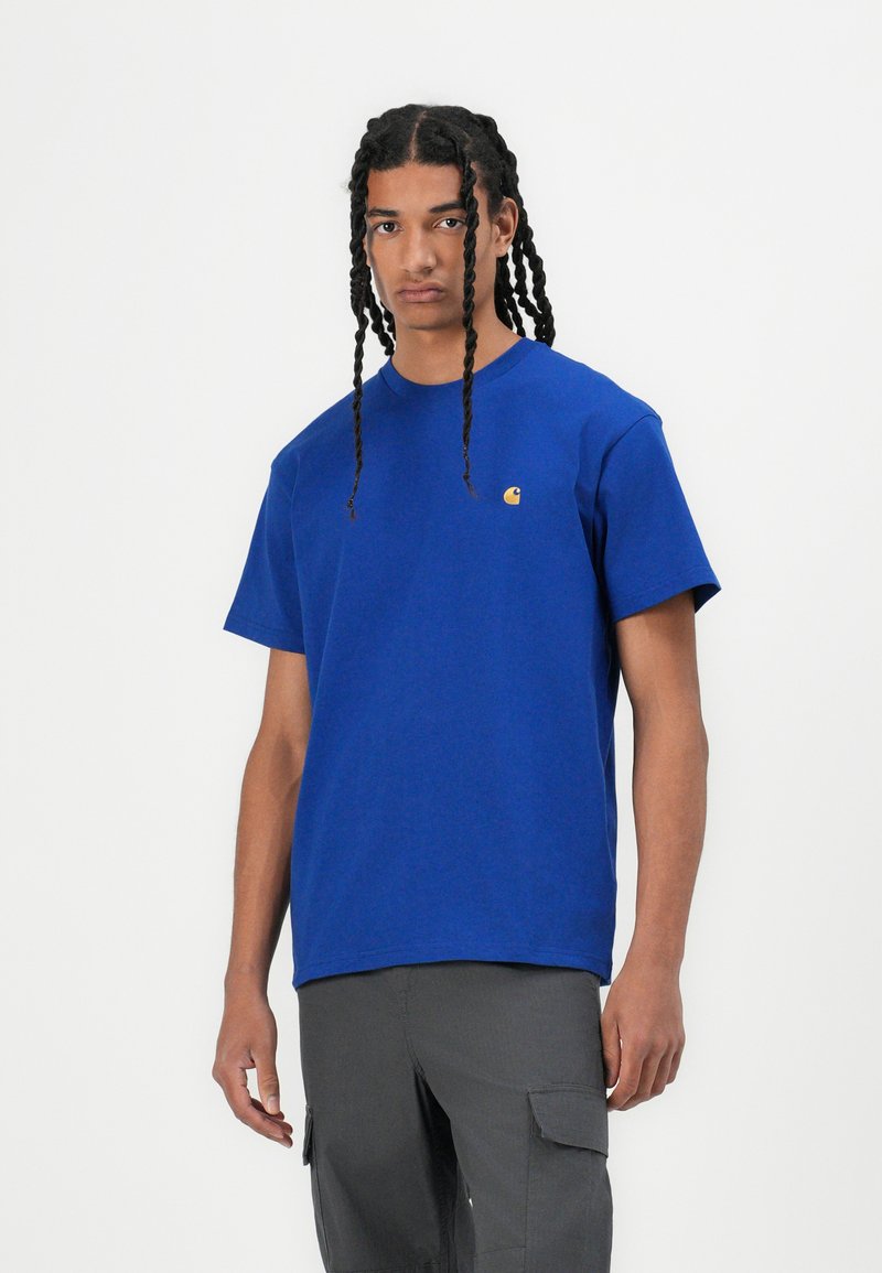 Blue cotton t-shirt with short sleeves, featuring a small yellow logo on the left chest. Smooth texture and classic crew neck design.