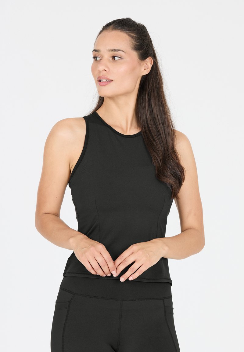 Zwarte mouwloze sporttop met een gladde textuur, aansluitend ontwerp, hoge halslijn en minimale stiksels. Draagt bijpassende high-waisted leggings.