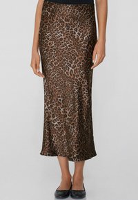 Jupe midi en satin à imprimé léopard avec une texture lisse, taille ajustée et silhouette fluide, portée avec des ballerines noires.