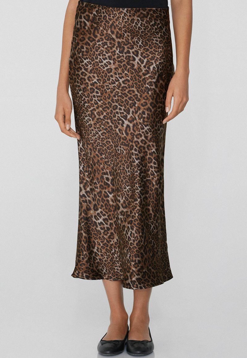 Jupe midi en satin à imprimé léopard avec une texture lisse, taille ajustée et silhouette fluide, portée avec des ballerines noires.
