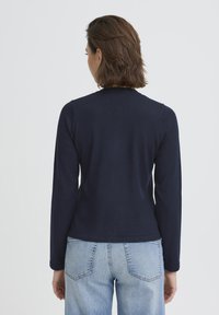 Haut à manches longues bleu marine en tissu doux, avec un col rond et une coupe ajustée, associé à un jean taille haute bleu clair.