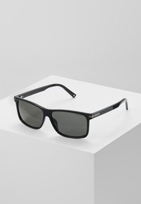 Ochelari de soare dreptunghiulari negri cu lentile gri, ramă din plastic lucios și accente metalice pe tempură. Design minimalist.