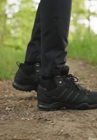 Czarne buty trekkingowe wykonane z materiału syntetycznego, z teksturowaną powierzchnią, wysokim wsparciem kostki i charakterystycznym wzorem w trzy paski.