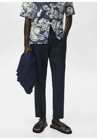 Cămașă cu imprimeu floral, cu mânecă scurtă, în nuanțe de albastru și crem; pantaloni navy pe comandă; șlapi negri; articol de îmbrăcăminte navy pliat în mână.