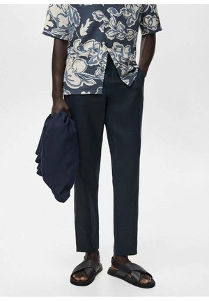 Camisa de manga corta con estampado floral en azul y crema; pantalones azul marino ajustados; chanclas negras; prenda azul marino doblada en la mano.