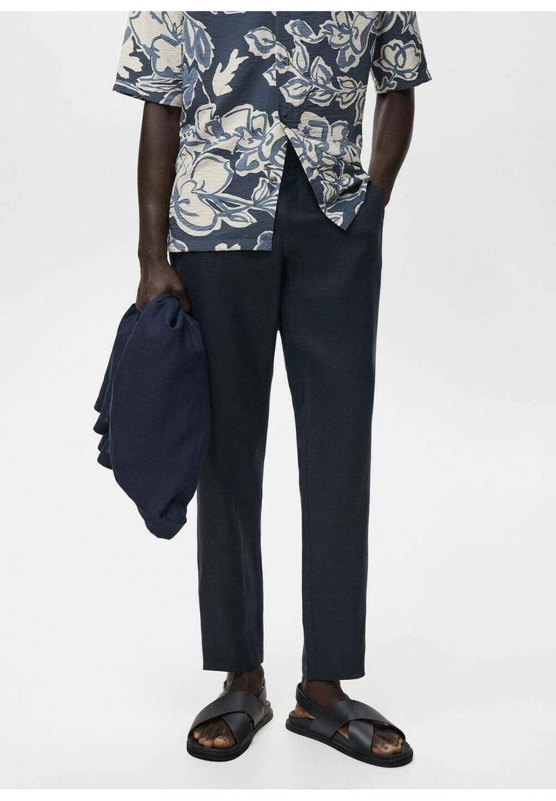 Cămașă cu imprimeu floral, cu mânecă scurtă, în nuanțe de albastru și crem; pantaloni navy pe comandă; șlapi negri; articol de îmbrăcăminte navy pliat în mână.