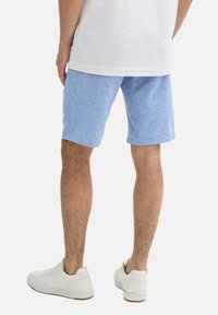 Pantalones cortos de color azul claro con una textura jaspeada, de largo hasta la rodilla, combinados con zapatillas blancas. Los pantalones cortos tienen un cinturón elástico y bolsillos laterales.