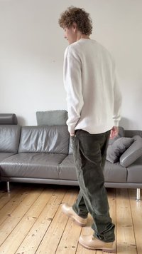 Bela pulover iz rebrastega pletenja, olivno zelene kordurove hlače in bež škornji. Enostaven dizajn s priložnostnim krojem na svetlem ozadju.