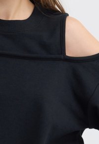 Sudadera negra con un diseño de hombro descubierto, cuello de canalé y textura suave, con detalles de costura visibles a lo largo de los hombros.