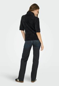 Suéter negro de manga corta y textura suave, con un alto cuello, combinado con jeans de denim oscuros. El suéter tiene una textura suave y un corte holgado.