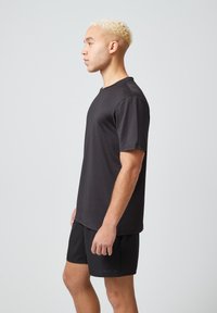 Czarny koszulek sportowy z krótkim rękawem z teksturowanej tkaniny, w połączeniu z czarnymi szortami. Prosty, funkcjonalny design, bez widocznych akcentów.