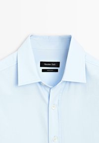 Camicia azzurra chiaro con colletto classico, con etichetta "Massimo Dutti" e bottoni bianchi lungo la parte anteriore. Tessuto morbido.