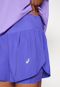 Μωβ αθλητική φούστα με στρωματοποιημένο σχέδιο, που διαθέτει διάτρητη υφή και λευκή λογότυπη λεπτομέρεια. Κατασκευασμένη από ελαφρύ, αεριζόμενο υλικό.